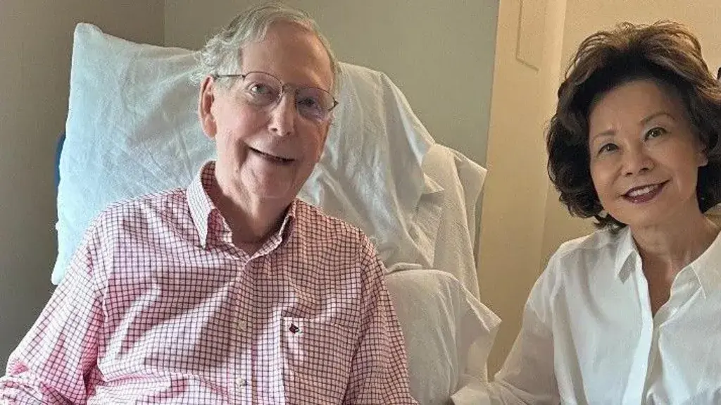 A photo of Mitch McConnell with his wife Elaine Chao. Mitch McConnell is in a medical bed that has been put in the upright position to help him sit up.